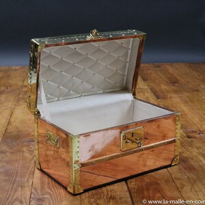 May include: An antique copper and brass travel trunk with a brass lock and hinges. The trunk is open and the interior is lined with a white fabric.