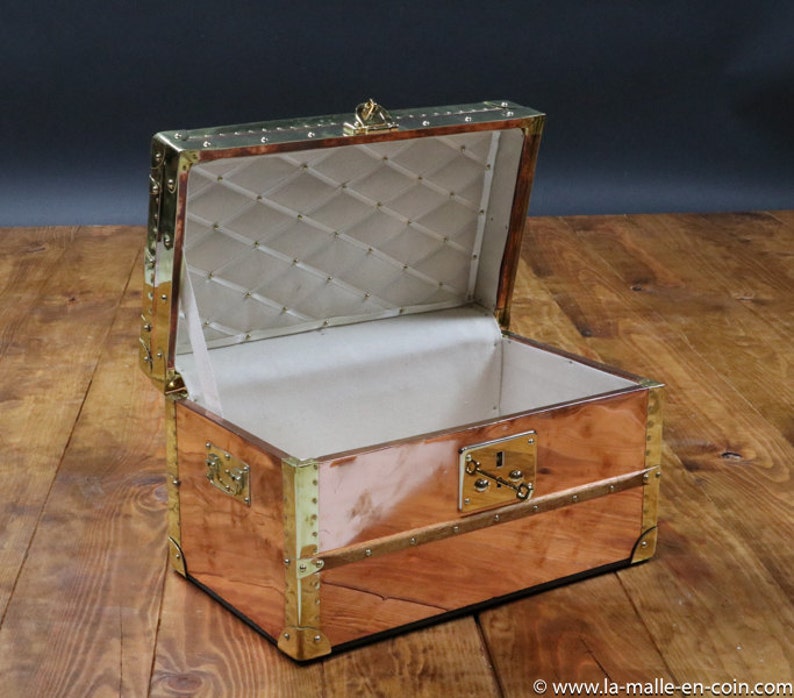 May include: An antique copper and brass travel trunk with a brass lock and hinges. The trunk is open and the interior is lined with a white fabric.