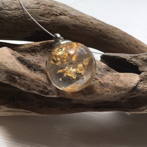 May include: A gold leaf pendant necklace with a clear resin oval charm. The pendant is hanging from a thin silver chain.