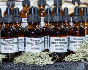 Könnte beinhalten: Eine Ansammlung von braunen Glasflaschen mit Tropfern, gefüllt mit dunkler Flüssigkeit, beschriftet mit "Vermont Usnea Tincture". Die Flaschen haben schwarze Tropfer und weiße Etiketten. Sie stehen vor getrocknetem, hellgrünem Moos.