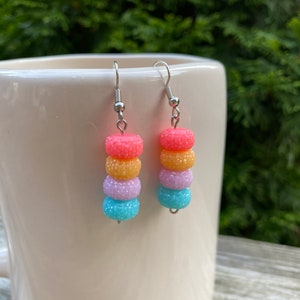 May include: A pair of dangle earrings with four colorful beads on each earring. The beads are pink, orange, purple, and blue.