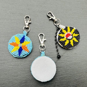 May include: Three beaded keychains with different designs. The first keychain has a blue, orange, and yellow beaded design. The second keychain has a black, white, red, and yellow beaded design. The third keychain has a plain white back.