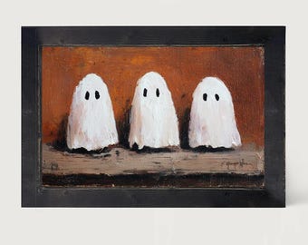 May include: An oil painting in a black wooden frame depicting three white ghosts with black eyes standing on a horizontal surface against a textured burnt orange background. The artwork features visible brushstrokes and a signature in the bottom right.