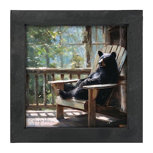 May include: A square framed painting depicting a black bear sitting upright in a wooden Adirondack chair on a porch. The scene features a forest background with sunlight filtering through the trees. The artist signature Ginger Blue is in the corner.