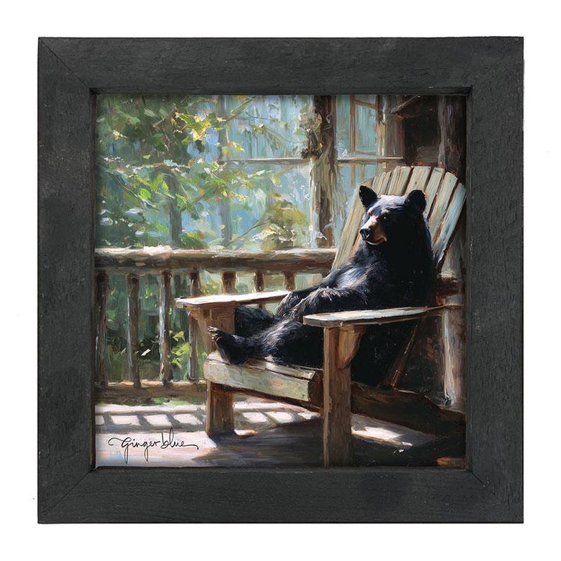 May include: A square framed painting depicting a black bear sitting upright in a wooden Adirondack chair on a porch. The scene features a forest background with sunlight filtering through the trees. The artist signature Ginger Blue is in the corner.