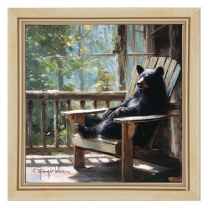 May include: A framed oil painting depicting a black bear sitting in a wooden Adirondack chair on a porch. The scene features sunlight filtering through green trees in the background. The artist signature Ginger Blue is visible in the bottom left corner.