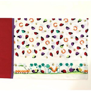 May include: White fabric with a repeating pattern of ladybirds, snails, and bees. The bottom border features a row of ladybirds, snails, and caterpillars on a green background.
