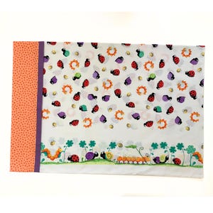 May include: White pillowcase with a colourful pattern of ladybirds, snails, bees, and flowers. The border of the pillowcase is orange with white polka dots and a purple stripe.