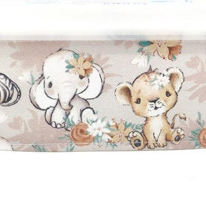 Könnte beinhalten: Ein beigefarbener Stoff mit einem sich wiederholenden Muster aus Zebra, Elefant und Löwe mit floralen Akzenten. Die Tiere sind im Cartoon-Stil mit braunen, weißen und schwarzen Farben illustriert.