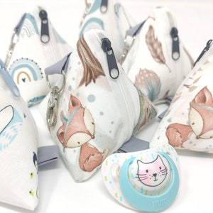 Könnte beinhalten: Ein Set aus sechs kleinen, dreieckigen Reißverschlusstaschen mit verschiedenen Tier- und Naturmotiven. Die Taschen sind aus weißem Stoff mit blauen, braunen und grauen Akzenten. Ein blauer und weißer Schnuller mit Katzenmotiv befindet sich im Vordergrund.