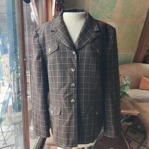 May include: A brown and white plaid blazer with a button-up front and two flap pockets. The blazer has gold buttons and a collar.