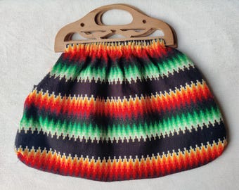 May include: A vintage handbag with a wooden handle. The bag features a colorful zig-zag pattern in shades of red, orange, green, and black. The handle is a light brown color and has a decorative cutout design.