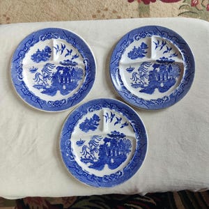 May include: Three blue and white divided plates with a Willow pattern design. Each plate features a central image of a pagoda, birds, and a bridge, with a decorative border. The plates are arranged on a white surface.