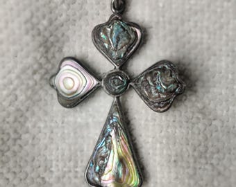 May include: A silver-toned metal cross pendant hanging from a matching chain. The cross features four distinct sections inlaid with iridescent abalone shell, displaying swirling patterns of green, blue, pink, and purple hues within a dark metal frame.