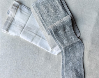 May include: A pair of gray patterned tights and a white folded cloth are displayed on a light-colored surface. The tights have a textured, open weave design. The cloth is white with subtle stripes.