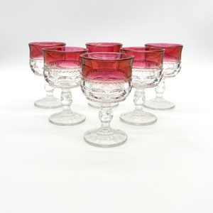 May include: Set of six clear glass stemmed wine glasses with a ruby red rim. The glasses have a textured pattern on the bowl and stem.