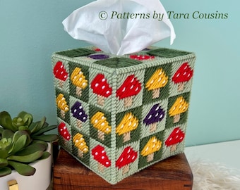 May include: A green tissue box cover with a checkered pattern of red, yellow, and purple mushrooms. The tissue box cover is made of plastic canvas and is a craft project.