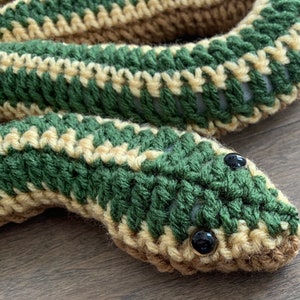May include: A crocheted green and tan snake with black eyes. The snake is curled up and has a textured surface.