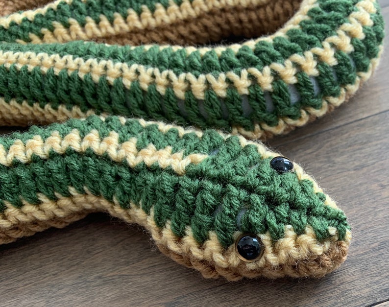 May include: A crocheted green and tan snake with black eyes. The snake is curled up and has a textured surface.