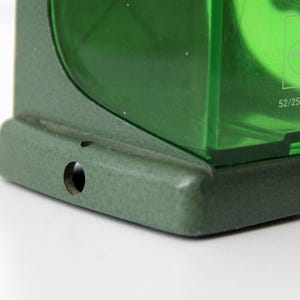Pu&ograve; includere: Una base in metallo verde con due fori di montaggio circolari sostiene un componente in plastica verde traslucida. La sezione in plastica presenta un logo stampato e il testo 52/25 GERMANY, con una finitura testurizzata sul telaio in metallo.