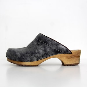 May include: A single gray clog shoe with a wooden sole. The upper part of the shoe is a dark gray, textured material. The wooden sole is a light brown color. The shoe is designed to be slipped on.