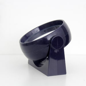 Peut inclure: Un miroir circulaire bleu marine foncé avec une finition lisse et brillante. Le miroir est monté sur un support assorti bleu marine foncé doté d'un mécanisme de charnière pivotant, permettant au cadre circulaire de s'incliner tout en restant fixé.