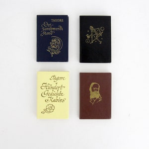 May include: Four small hardcover books with gold-embossed designs. The top left is dark blue with text reading Tagore Der Zunehmende Mond. The top right is black with a figure. The bottom left is yellow with text Tagore Hundert Gedichte Kabirs. The bottom right is maroon with a portrait.