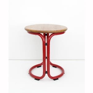 May include: A small, round side table with a wooden top and a red metal frame. The table has a unique, curved leg design and stands approximately 20 inches tall.