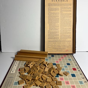 May include: A vintage Scrabble board game with wooden letter tiles scattered across the board. The game board features a grid with colored squares for bonus points. The box lid displays the rules for playing Scrabble.
