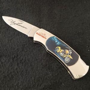May include: A silver pocket knife with a black handle featuring a motorcycle graphic and the text "Easy Riders". The knife has a silver blade with the signature "Jay Leno" engraved on it.