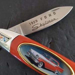 May include: A pocket knife with a red handle and a silver blade. The blade is engraved with "1959 FORD Skyliner." The handle features a picture of a classic red and white car. The Ford logo is visible on the handle.