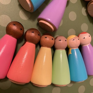 May include: A set of eight wooden peg dolls with painted faces and colorful dresses. The dolls are arranged in a semi-circle, with the tallest doll in the center.
