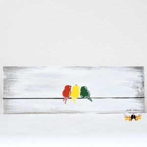 May include: A rectangular wooden sign with a distressed white finish featuring a thin black horizontal line. Three stylized birds in red, yellow, and green are perched on the line. The text Linda Fehlner Gallery is printed in the bottom right corner.