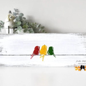 May include: A rectangular white wooden sign with a distressed finish featuring a painted illustration of three birds in red, yellow, and green perched on a thin black line. The text Linda Fehlor GALLERY is printed in the bottom right corner.