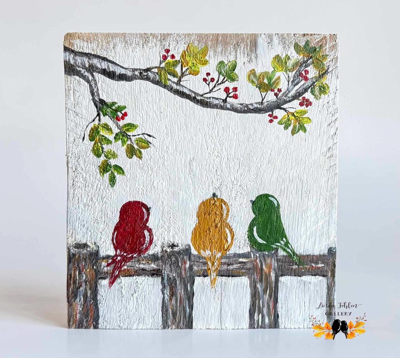 May include: A rectangular wooden plaque featuring a hand-painted scene of three birds in red, yellow, and green perched on a brown fence. Above the birds, a tree branch with green leaves and red berries extends across the white-washed wood surface.