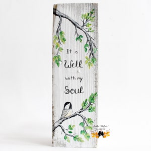 wood wall art featuring a sweet chickadee bird sitting on a tree branch with leaves that are shades of green and yellow, another branch hangs from above perfectly framing the comforting phrase It is Well with my Soul