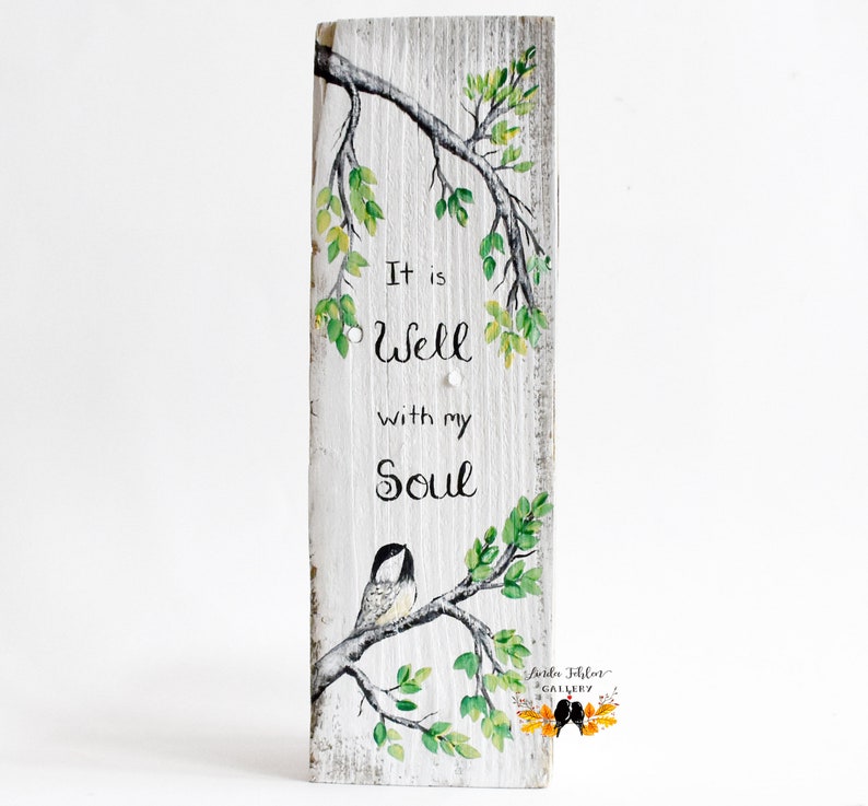 wood wall art featuring a sweet chickadee bird sitting on a tree branch with leaves that are shades of green and yellow, another branch hangs from above perfectly framing the comforting phrase It is Well with my Soul
