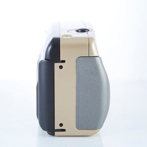 May include: A gold and black compact point-and-shoot camera with a silver lens cover.