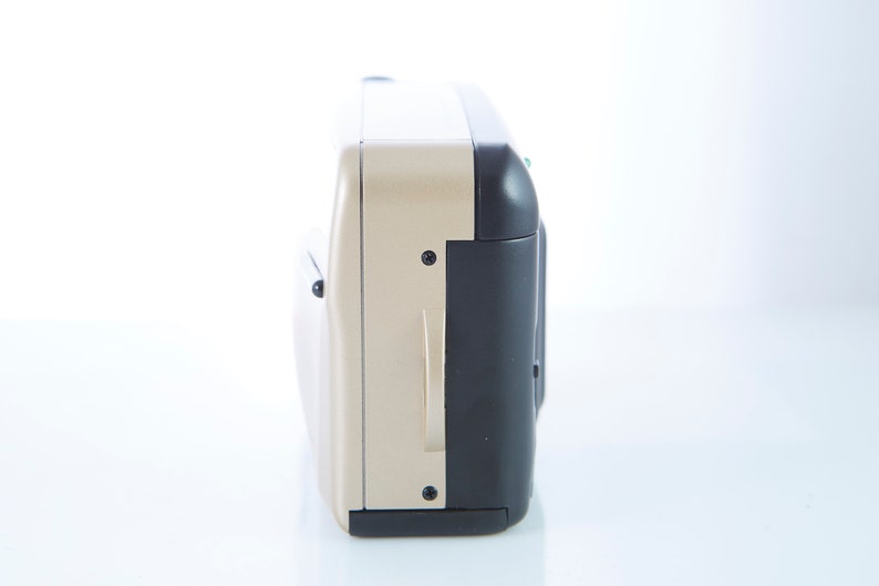 May include: A gold and black compact camera with a built-in flash. The camera has a small LCD screen on the back.