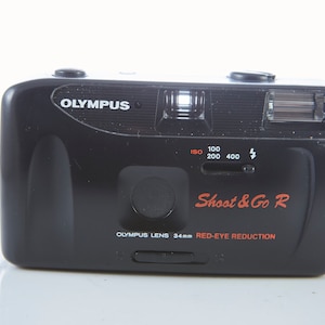 Könnte beinhalten: Schwarze Olympus Shoot & Go R 35mm Filmkamera mit einer Funktion zur Reduzierung von Rote-Augen-Effekten und einem 34mm Objektiv.