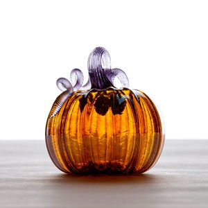 May include: A glass pumpkin with a purple stem and a textured amber finish.