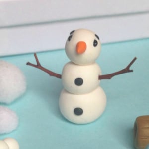 May include: A white snowman figurine with black eyes and a small orange nose. The snowman has two arms made of brown twigs.