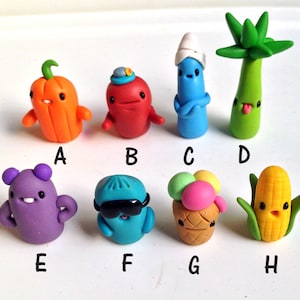 May include: A set of 8 colorful handmade polymer clay figurines. The figurines are shaped like a pumpkin, a red character with a hat, a blue character with a white hat, a green plant, a purple character, a blue character with sunglasses, an ice cream cone, and a yellow corn cob.