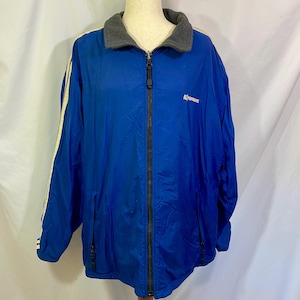 May include: A blue zippered jacket with white stripes on the sleeves and a gray fleece lining. The jacket has a logo that says "Adventure" on the front.