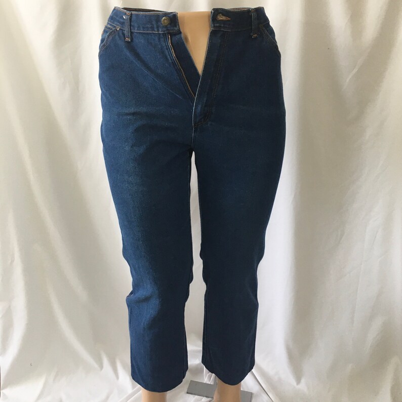 Op de afbeelding: Een paar donkerblauwe spijkerbroeken met een ritsvlieg en knoopsluiting. De broek heeft een rechte pijp en een verkorte lengte.