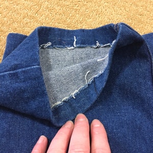 Op de afbeelding: Close-up van de binnenkant van een blauwe denim jackenkraag, die de rauwe rand van de naad en de stiksels laat zien.