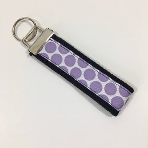 May include: A black and white key chain with a purple polka dot pattern. The key chain has a silver metal ring and a black fabric strap.