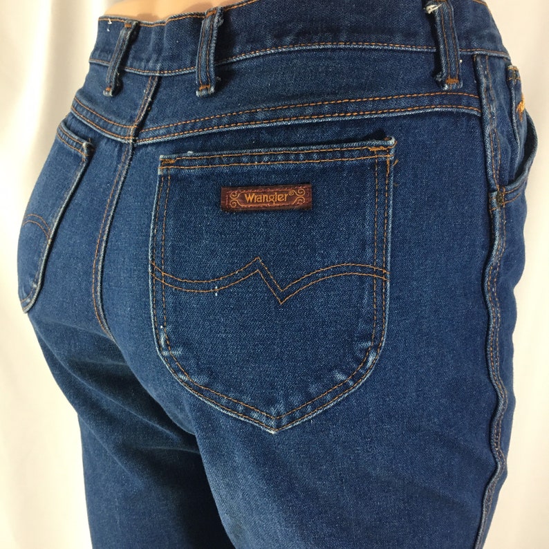 Op de afbeelding: Een paar blauwe denim jeans met een bruin leren patch met daarop "Wrangler" op de achterzak.