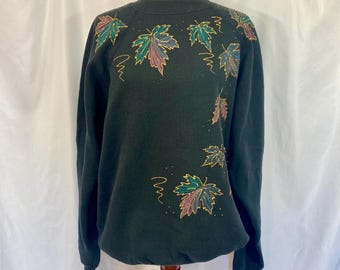 May include: A black sweatshirt with a colorful leaf design. The leaves are outlined in gold and have shades of green, purple, and pink.