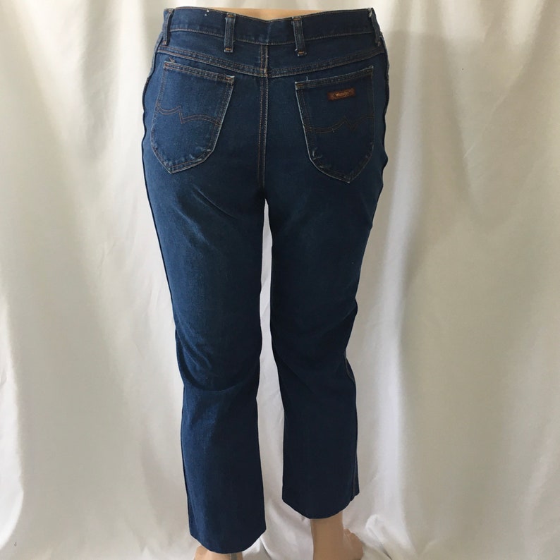 Op de afbeelding: Donkerblauwe denim jeans met een rechte pijp. De jeans heeft een hoge taille en een klassieke vijf-zak stijl. De achterzakken hebben een bruin leren patch met het Wrangler logo.